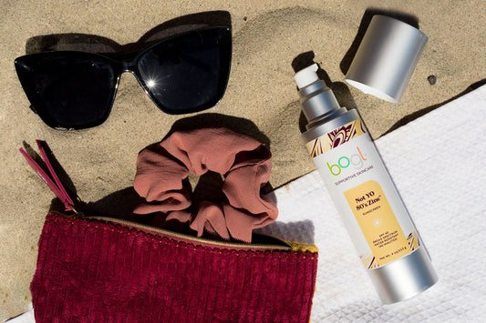 sunglasses, makeup bag and SPF on sand